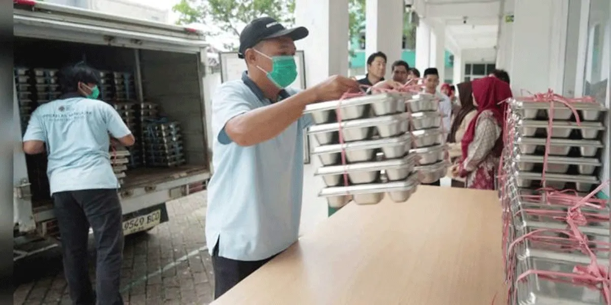Petugas dapur MBG sedang mengangkat ompreng berisi makanan sebelum didistribusikan ke penerima manfaat.