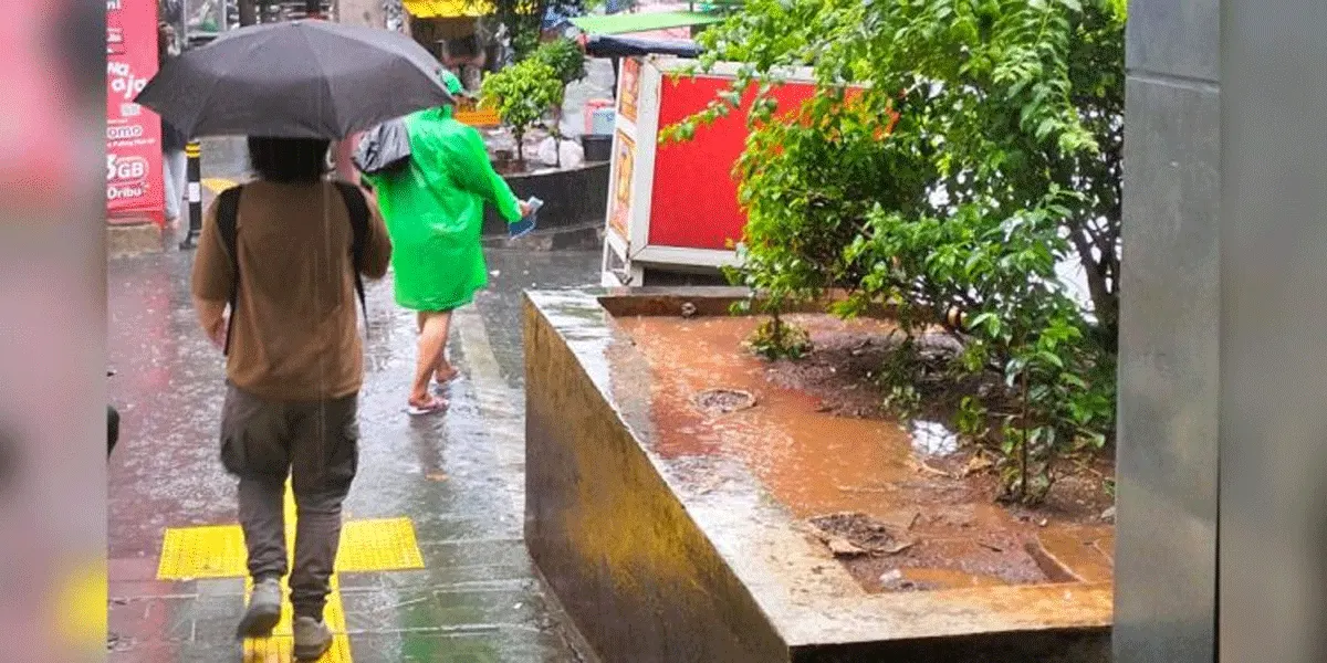 Pejalan kaki menyusuri trotoar saat hujan di Jakarta.